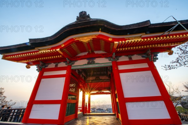 Sunset over the city with sun stars, view through the red Nishimon Gate, Kiyomizu-dera Temple, in