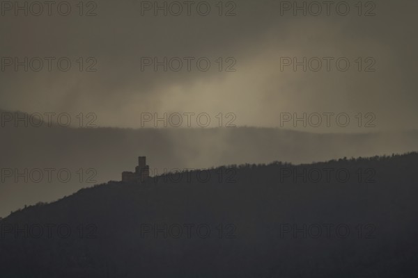 The structure is on a mountain. The sky is cloudy and sunlight is shining in the distance. The