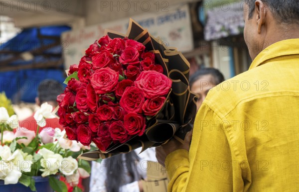 A customer holds a bouquet of red roses at a flower shop on Valentine's Day in Guwahati, India, on