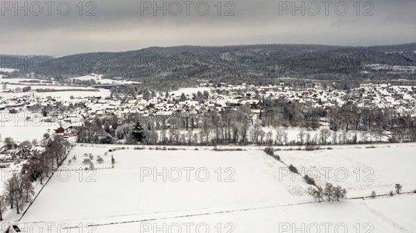 Aerial view of a snowy landscape with fields, hills and a village under grey sky, Herleshausen in