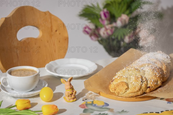 Yeast braid is sprinkled with sugar, breakfast table with coffee and decoration for Easter