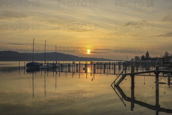 Atmospheric sunrise scene with calm water and sailboats on the jetty, Lake Constance, Überlinger
