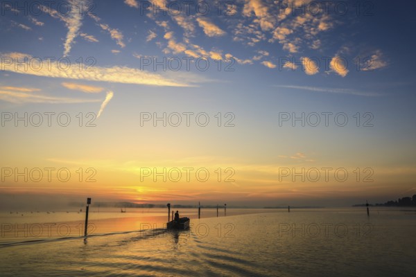 A fishing boat glides through Lake Zell at sunrise, the sky is decorated with clouds, moss, Höri