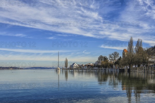 Calm lake in winter with a sailboat on the shore, surrounded by houses and trees, under a cloudy