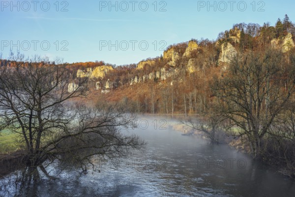 Picturesque river landscape with foggy water, surrounded by autumn trees and imposing Jurassic