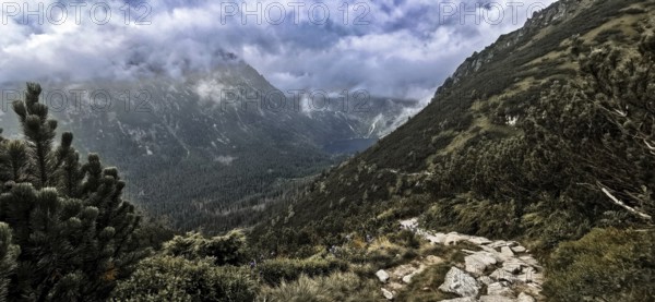 Wild mountain trail with a view of a lake, Morskie Oko and thick, dramatic clouds above the peaks,