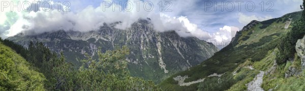 A trail leads through impressive mountain scenery, panoramic peaks covered with green slopes and
