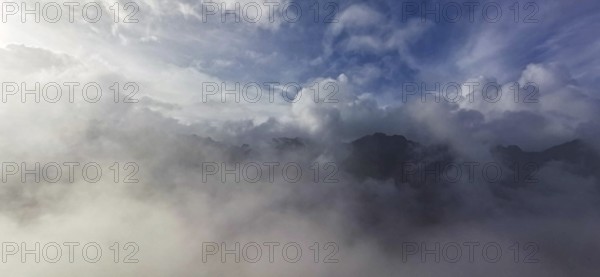 Atmospheric scene with clouds and fog over a mountain landscape under blue sky, hiking in the High