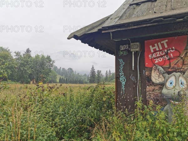 Old hut structure with poster with a cartoon mouse in the midst of a grassy landscape and cloudy