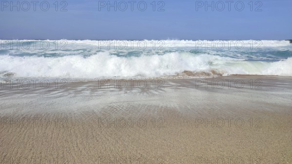 Empty sandy beach with breaking waves under clear blue skies, hiking on the Fisherman's Trail,