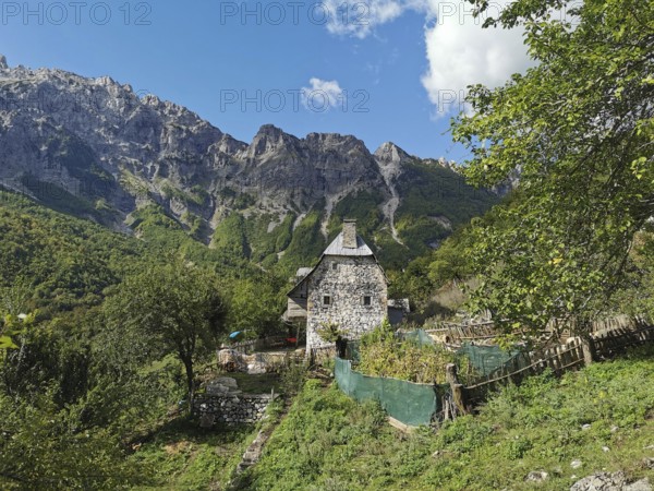Stone house surrounded by gardens and mountains under a clear blue sky, Peaks of the Balkans,