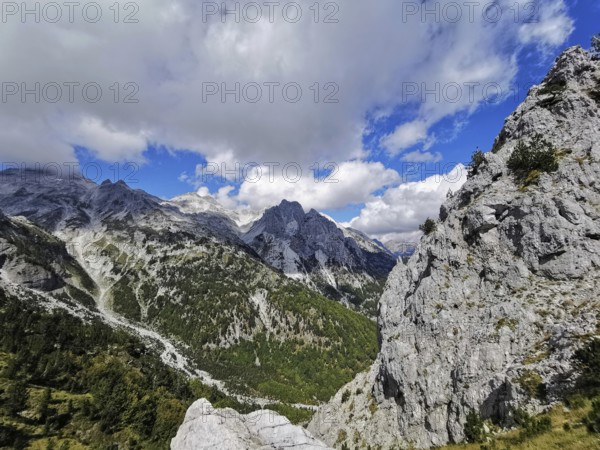 Rugged mountain landscape with clouds and blue sky, trees on rocky hillside, Peaks of the Balkans,