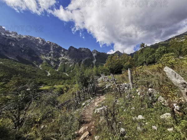 Rocky hiking trail along a hill surrounded by mountains under rugged skies, Peaks of the Balkans,