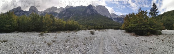 Panorama, wide riverbed in front of a wooded mountain landscape under blue sky and clouds, Peaks of