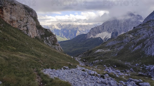 View of a rocky valley surrounded by imposing mountain ranges under a partly cloudy sky, Peaks of