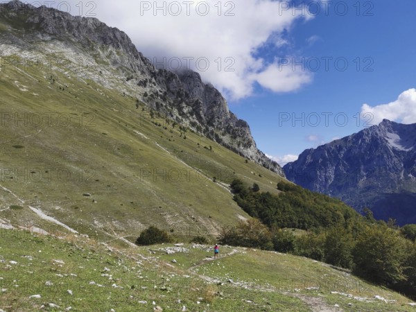 Extensive alpine landscape under a cloudy sky next to imposing mountain slopes, Peaks of the