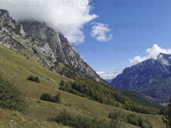 Quiet mountain meadow below impressive rock formations with clear skies, Peaks of the Balkans,