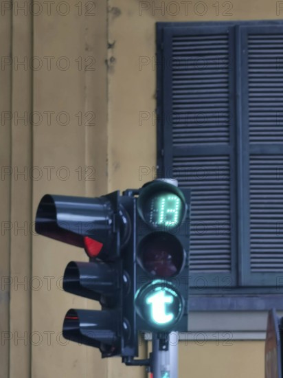 Close-up of a green traffic light in Tirana green letter T in front of a building with shutters