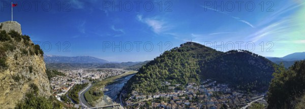 Panorama, view of a castle on a hill with Albanian flag with river and city in the valley under a