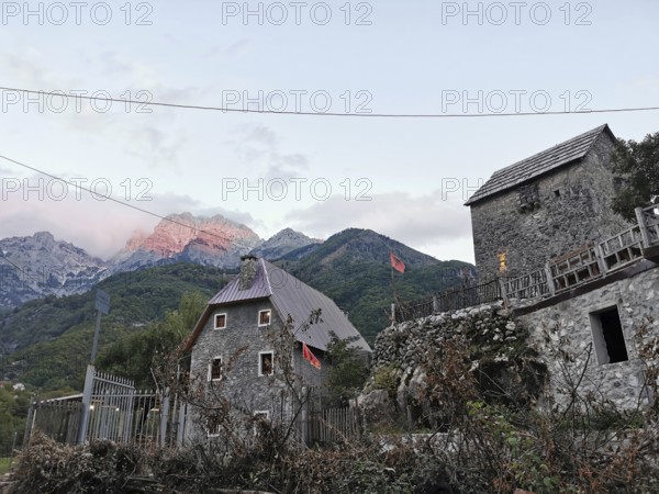 Traditional village with stone houses and Albanian flags against a mountain backdrop, mountain
