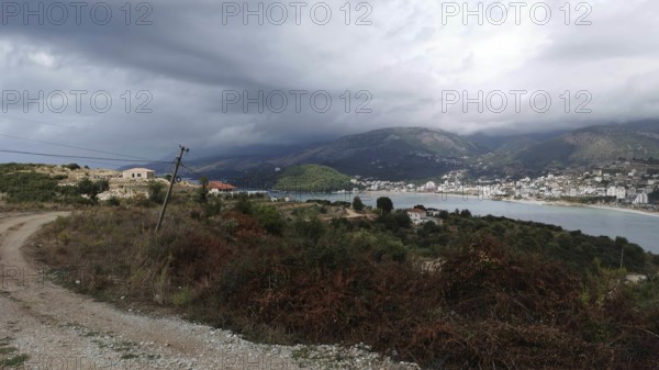 Hilly coastal landscape with a path by the sea and a village on a mountainside under cloudy sky,