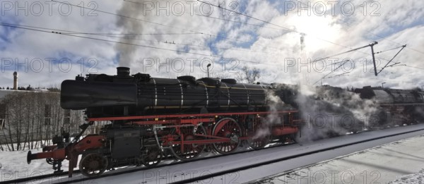 A historic steam locomotive emits smoke while standing on tracks in winter, Rennsteig, Frankenwald