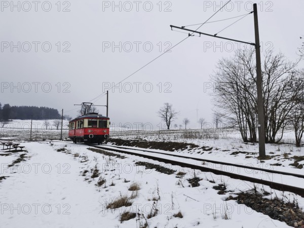 A red train travels through a snow-covered landscape, snow-covered fields in the background,