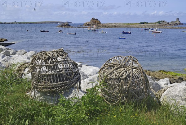 Large rope rolls lie on the shore with a wide view of the sea and several boats, lobster cages, St