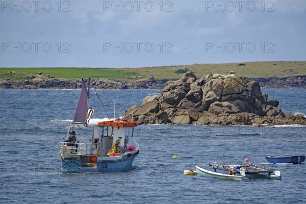 A small fishing boat out at sea off a rocky coast with colorful sails and clear skies, St Agnes,