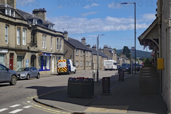 Urban street scene with cars and buildings under blue sky, Dufftown, Aberdeenshire, Scotland,