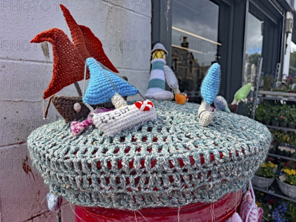 Colourful crocheted motifs of ships and houses on a wall in a maritime scene placed on a letterbox,