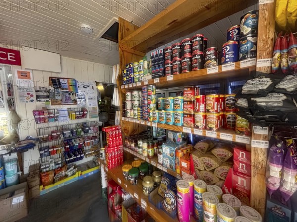 A small shop with stocked shelves full of cans and colorful food products, the only shop in the