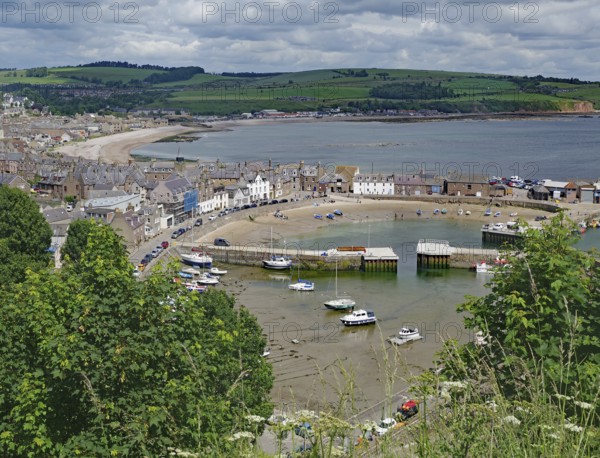 Coastal view of a village with harbour, boats and green hills under a cloudy sky, Stoneheaven,