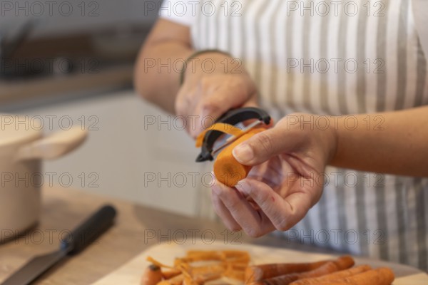 Close up of hands peeling fresh carrot in home kitchen. Healthy ingredients, simple food