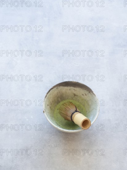 Matcha green tea with bamboo whisk in a ceramic bowl on a concrete background