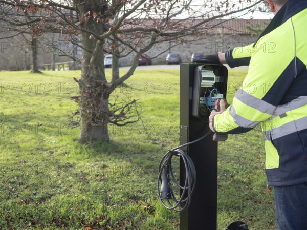 Worker installing electric vehicle charging station, connecting wires in the open panel