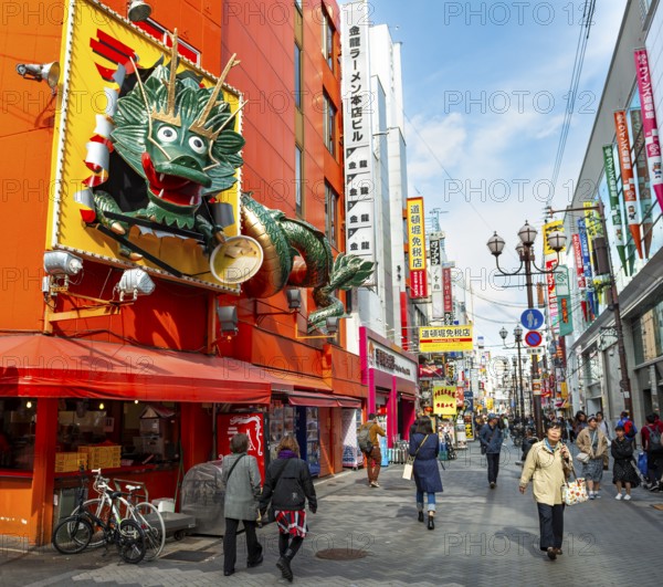 Dragon figure at a restaurant, lots of colorful signs in a pedestrian zone with shops and