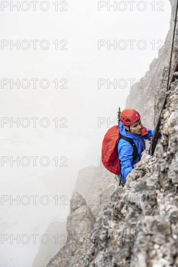 Mountaineers on a ladder on the Via Ferrata Oliva Detassis via ferrata in fog, rocky mountain peaks