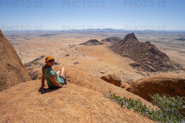 Woman sitting on rocks and enjoying the view over the barren desert landscape of Spitzkoppe,