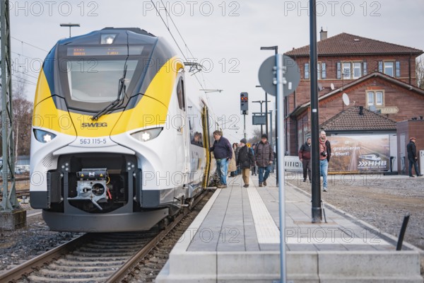 A train on the platform with people and buildings in the background, opening of the Hermann Hesse