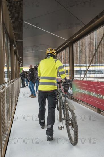 Cyclist wearing yellow safety clothing pushes a bicycle across a modern bridge, opening of the