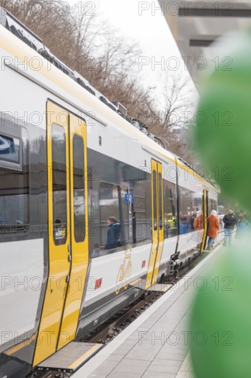 A yellow and white train stands on the platform with people and green balloons, opening of the