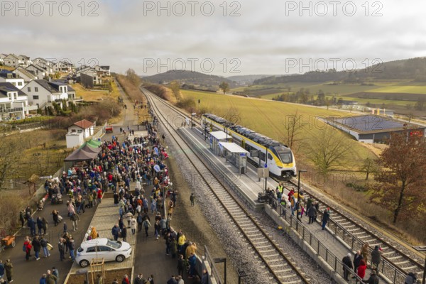 A lively train station in a rural area with lots of people, trains and an idyllic landscape,