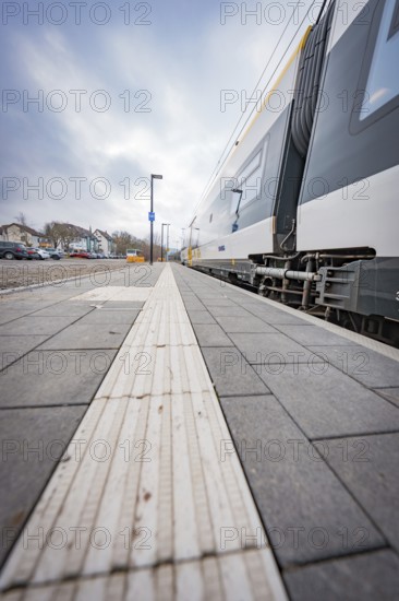 View along an empty sidewalk at a train station under a grey sky, opening of the Hermann Hesse