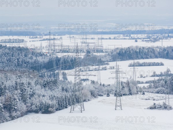 Snow-covered fields with electricity poles and a village in the background under a blue sky,