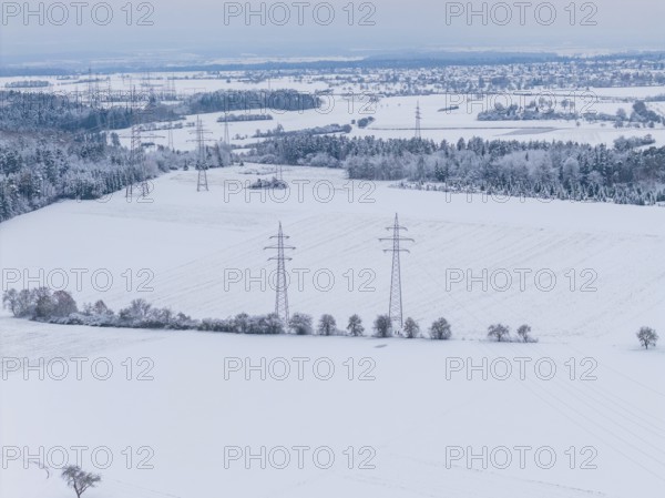 Wide snow-covered fields with power lines and small villages on the horizon in cold weather,