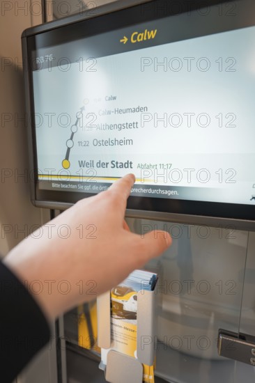 Hand points at a display with timetable and departure times on the train, battery electric train