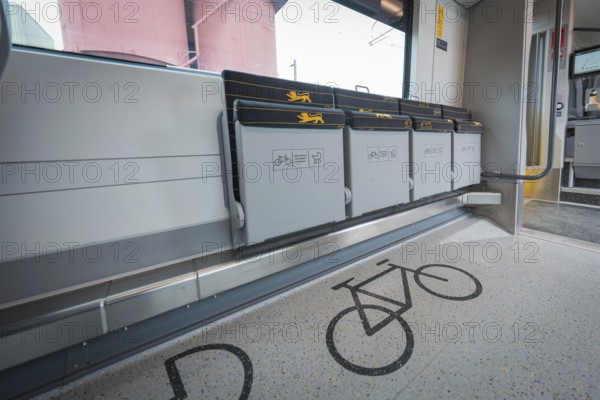 Train compartment with marked bicycle parking spaces and grey folding seats, battery electric train