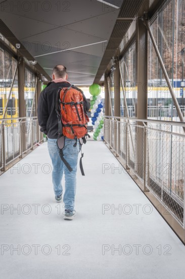 Man with orange backpack walks across a glazed transition with balloons, battery electric train