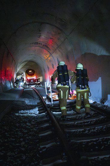 Firefighters walk on tracks through a dark tunnel with red light effects, fire drill on the Hermann